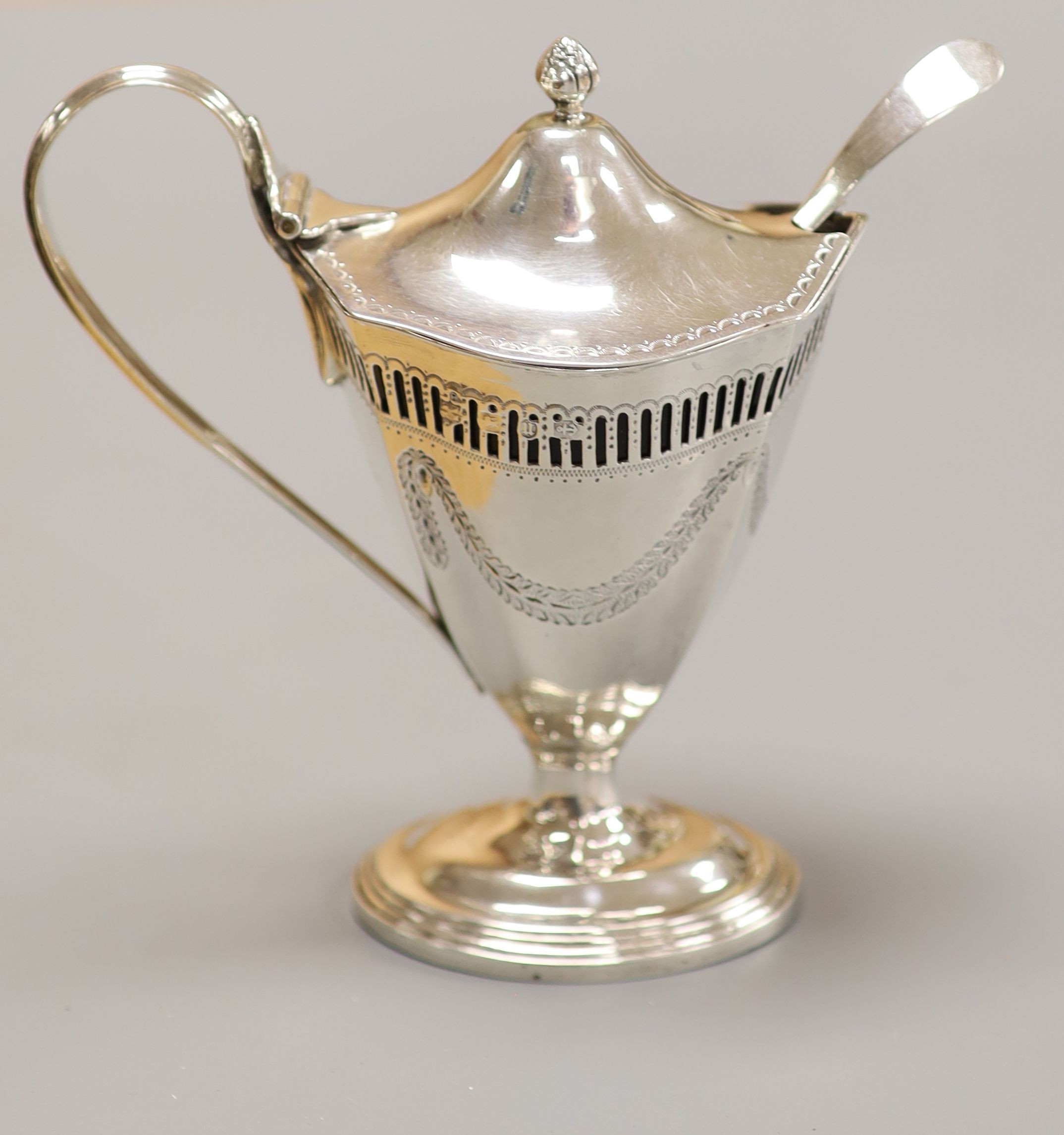 A late Victorian pierced and engraved silver vase shaped pedestal mustard, Nathan & Hayes, Birmingham, 1894, with blue glass liner and an earlier Georgian mustard ladle, height 13.2cm, 147 grams.